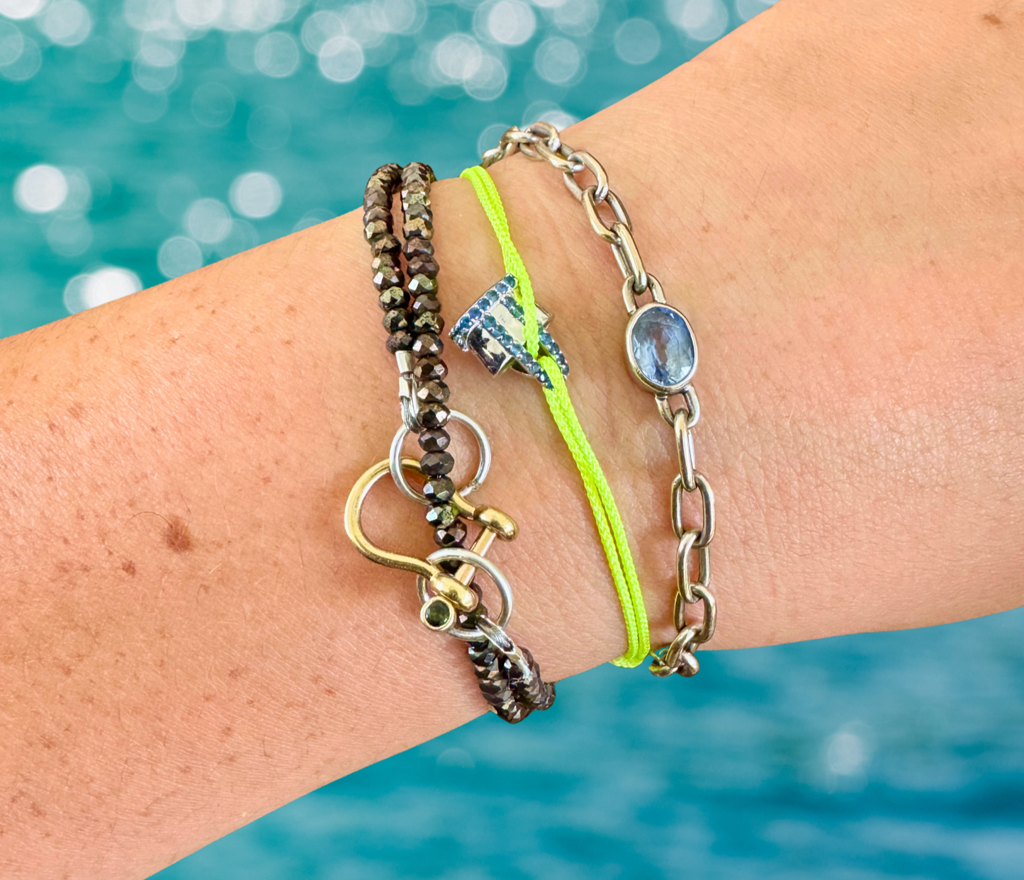 Close-up of a wrist wearing multiple bracelets with a blurred blue water background