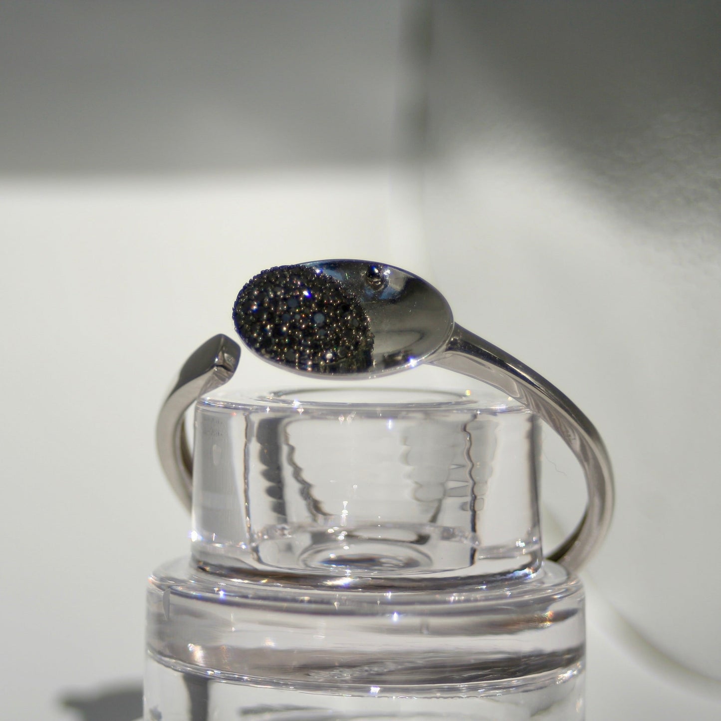 Silver bracelet with a black gemstone on a clear stand against a neutral background
