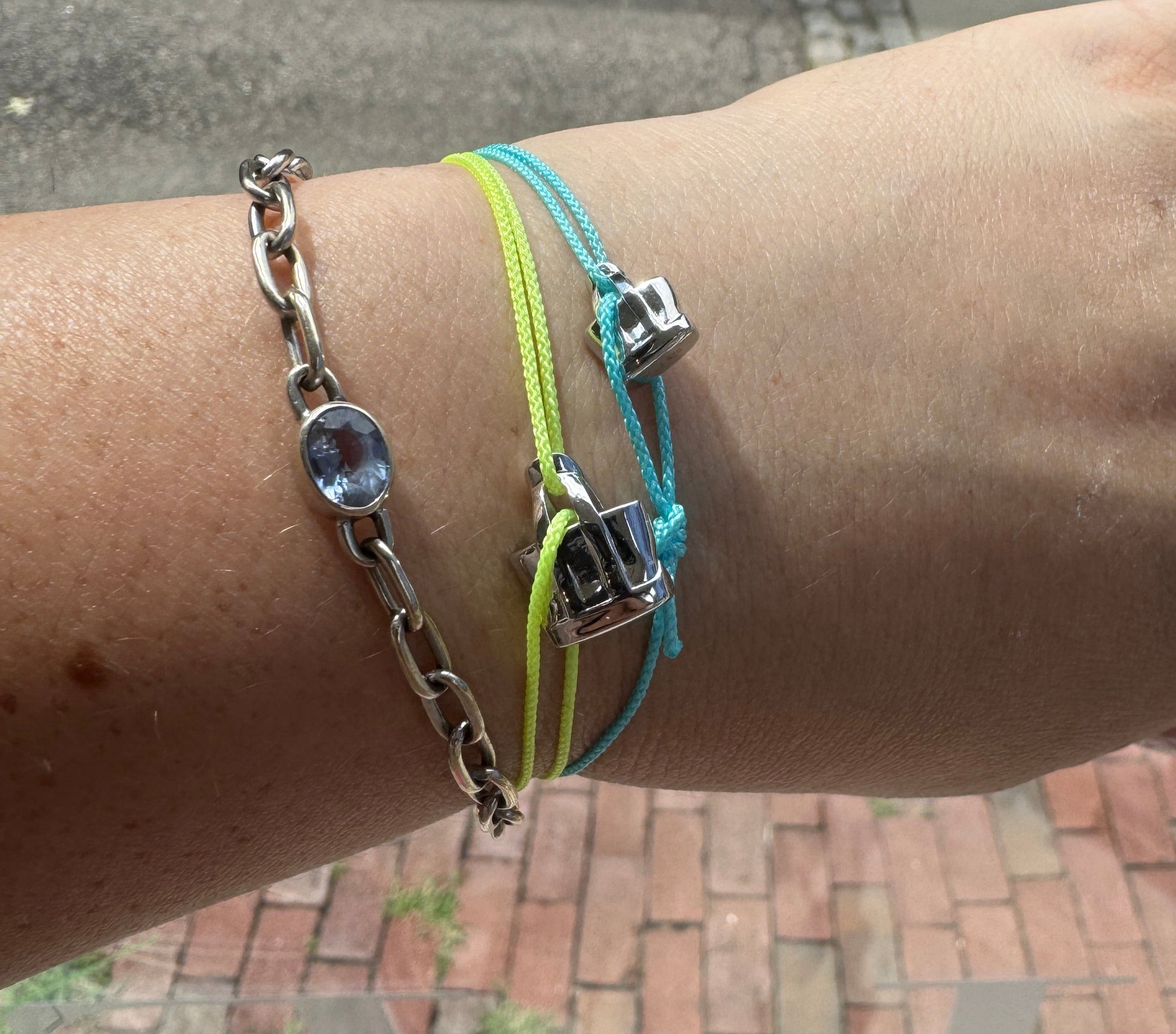 Hand wearing multiple bracelets with a brick wall background