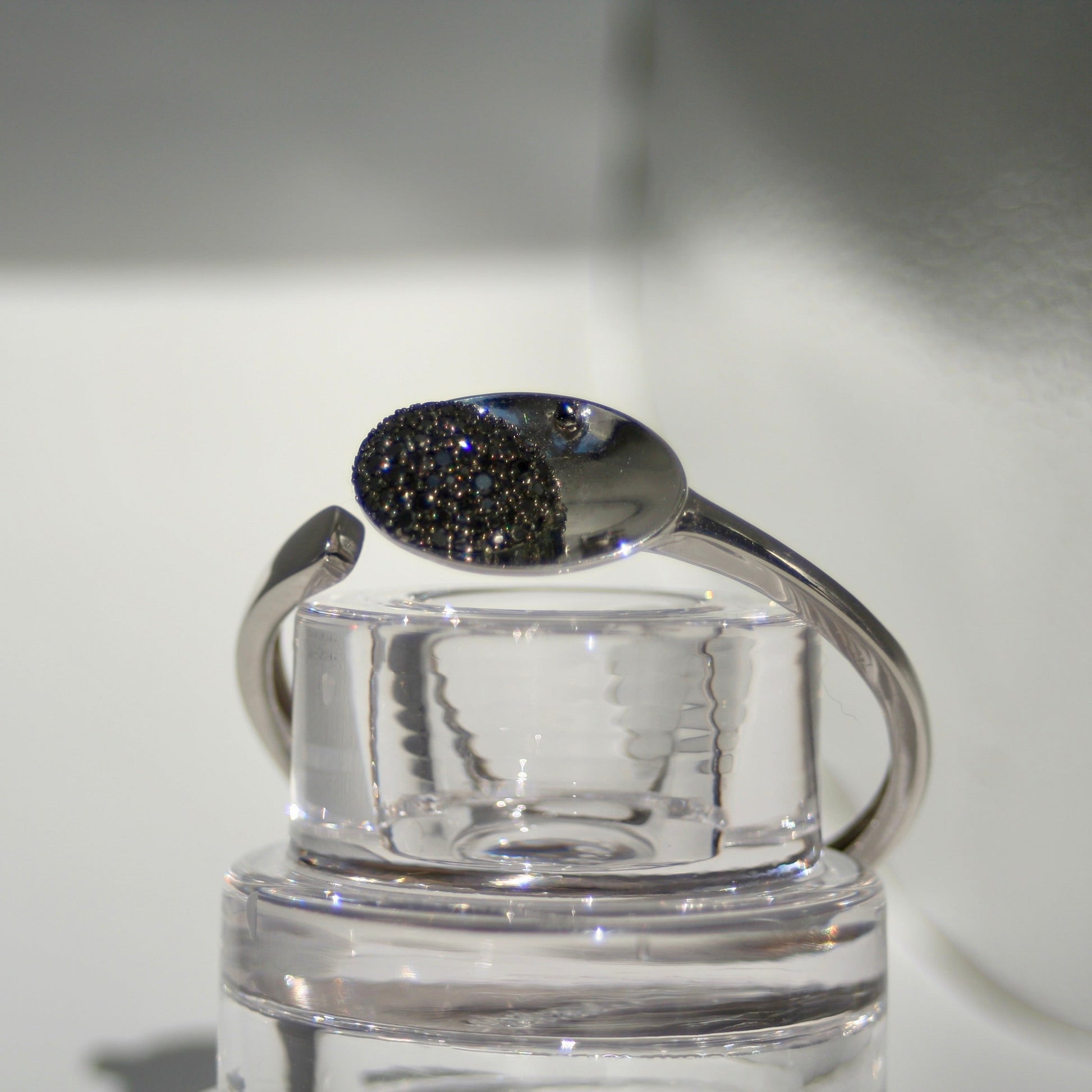 Silver bracelet with a black gemstone on a clear stand against a neutral background