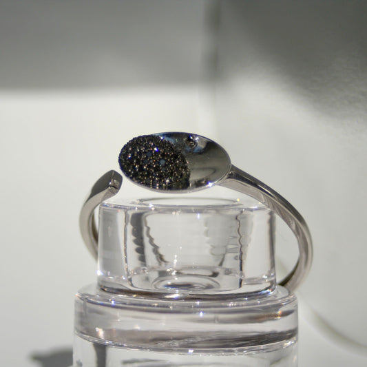 Silver bracelet with a black gemstone on a clear stand against a neutral background
