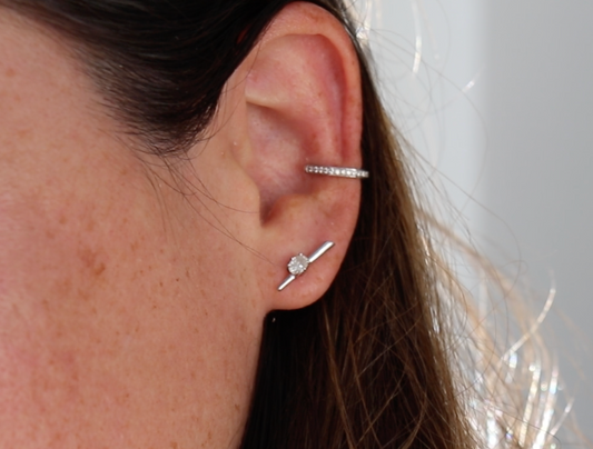 Close-up of an ear wearing a silver earring with a clear gemstone on a neutral background